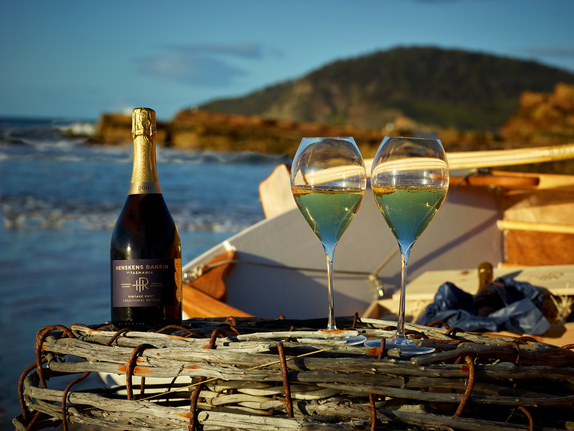 Bottle of Henskens Rankin Wine and two glasses sitting atop a crayfish pot on the beach